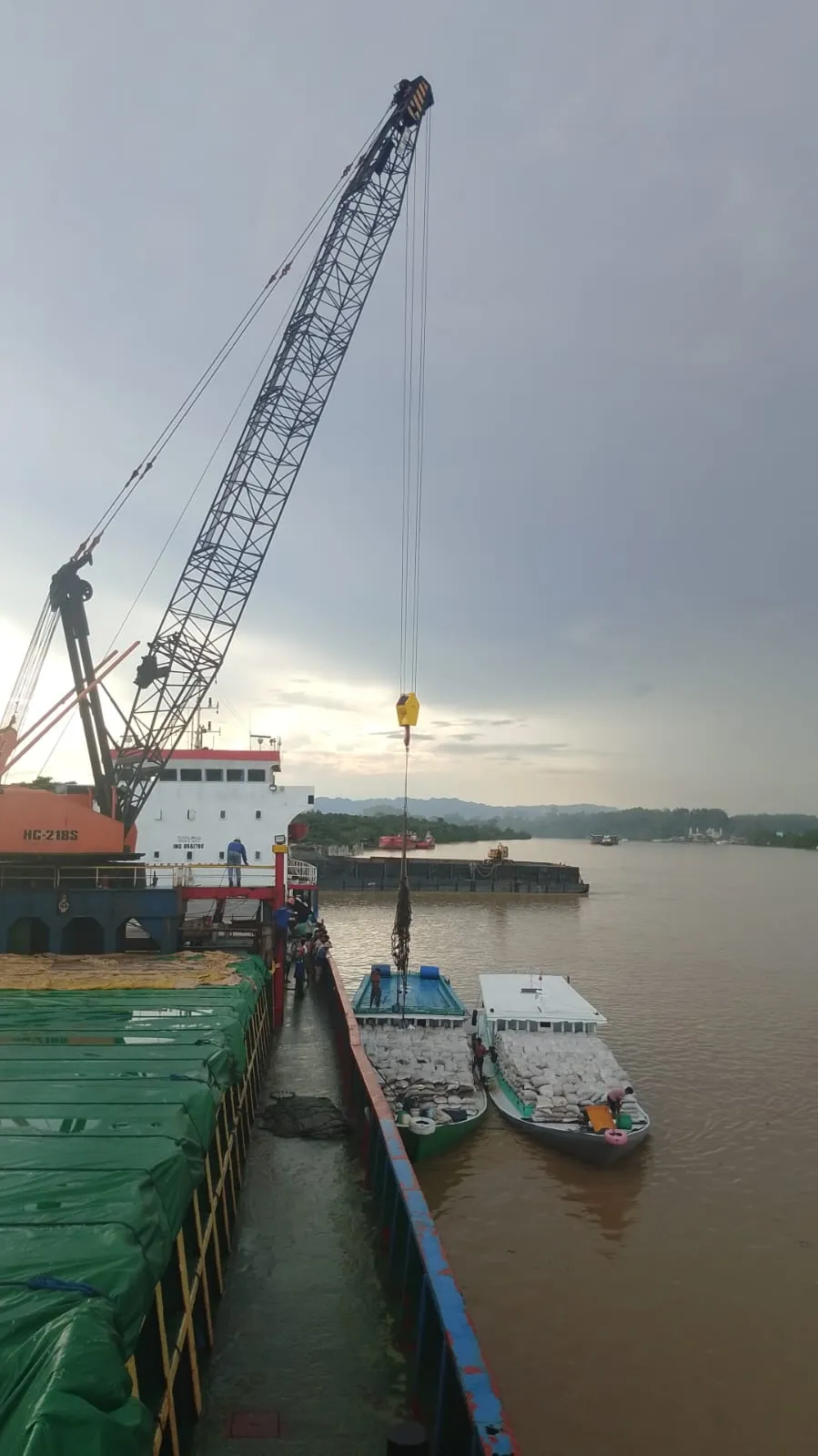 Crane mengangkat muatan dari kapal ke perahu kecil di sungai