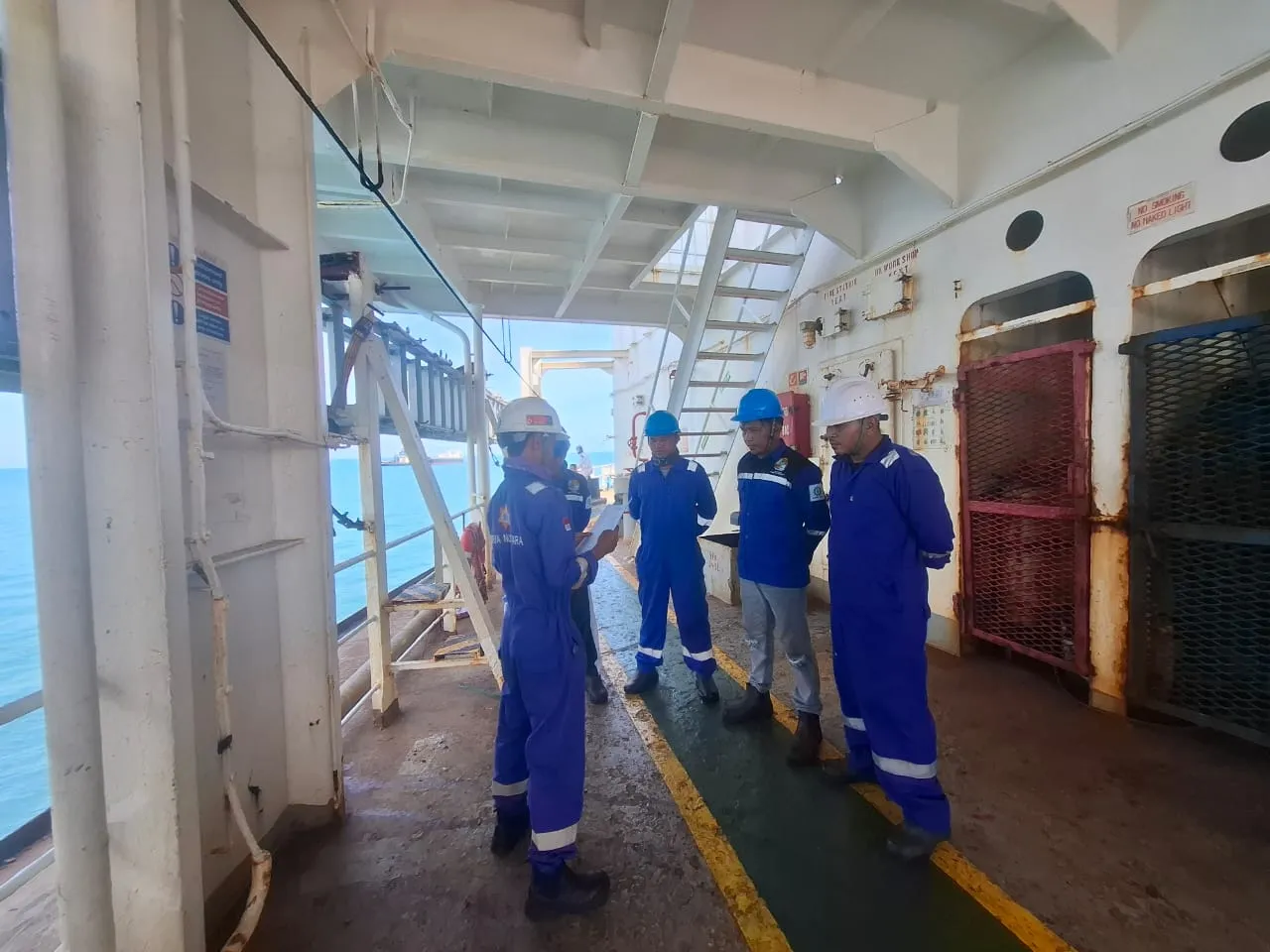 Lima anggota tim berseragam biru dan berhelm keselamatan di geladak kapal